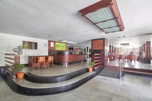 A hotel lobby with a reception desk, seating area, and a staircase leading to another level. - Bharat Hotel (Kanayannur)