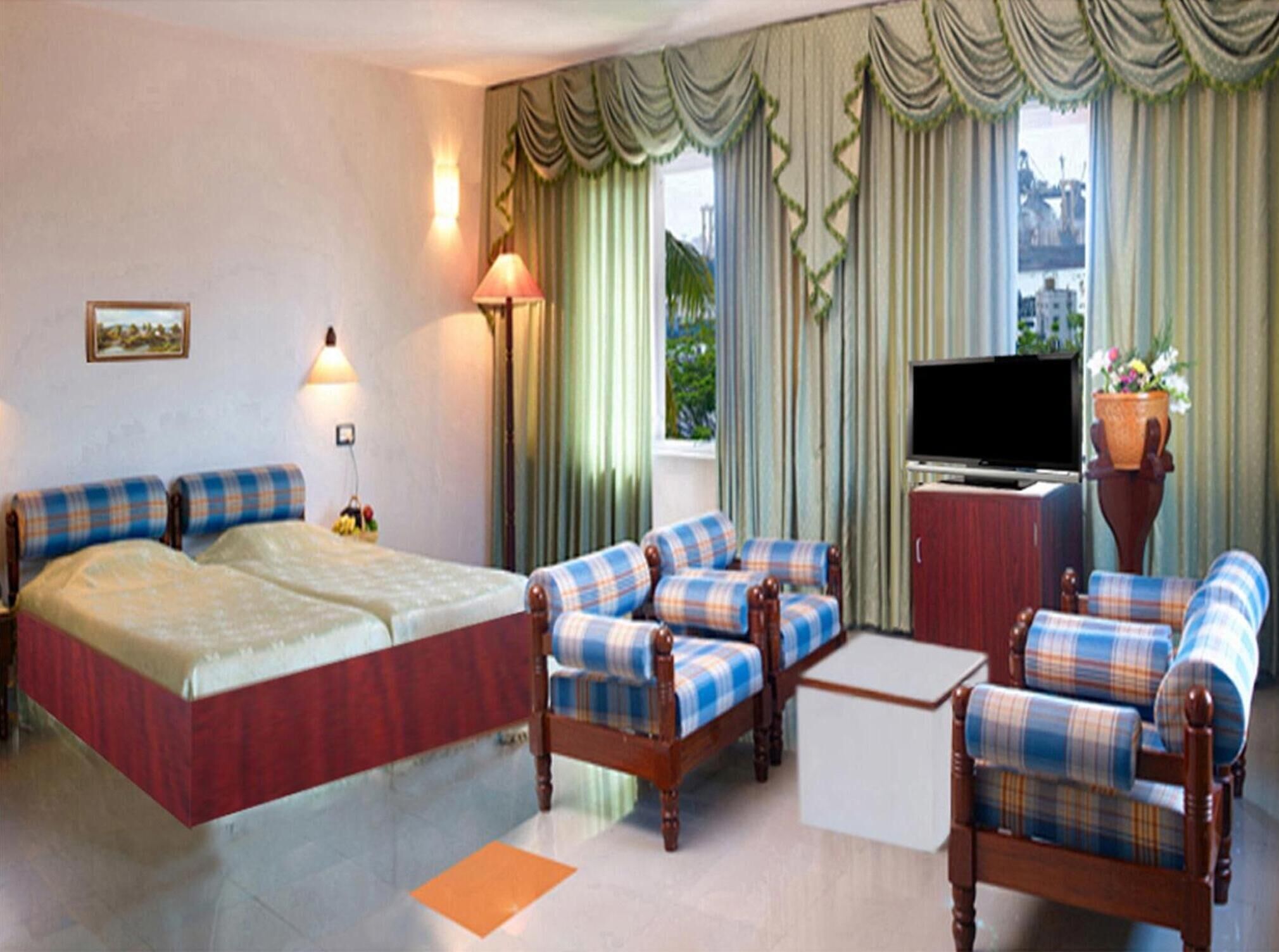 Une chambre d’hôtel avec un lit, deux fauteuils, un canapé, une télévision et une plante en pot.