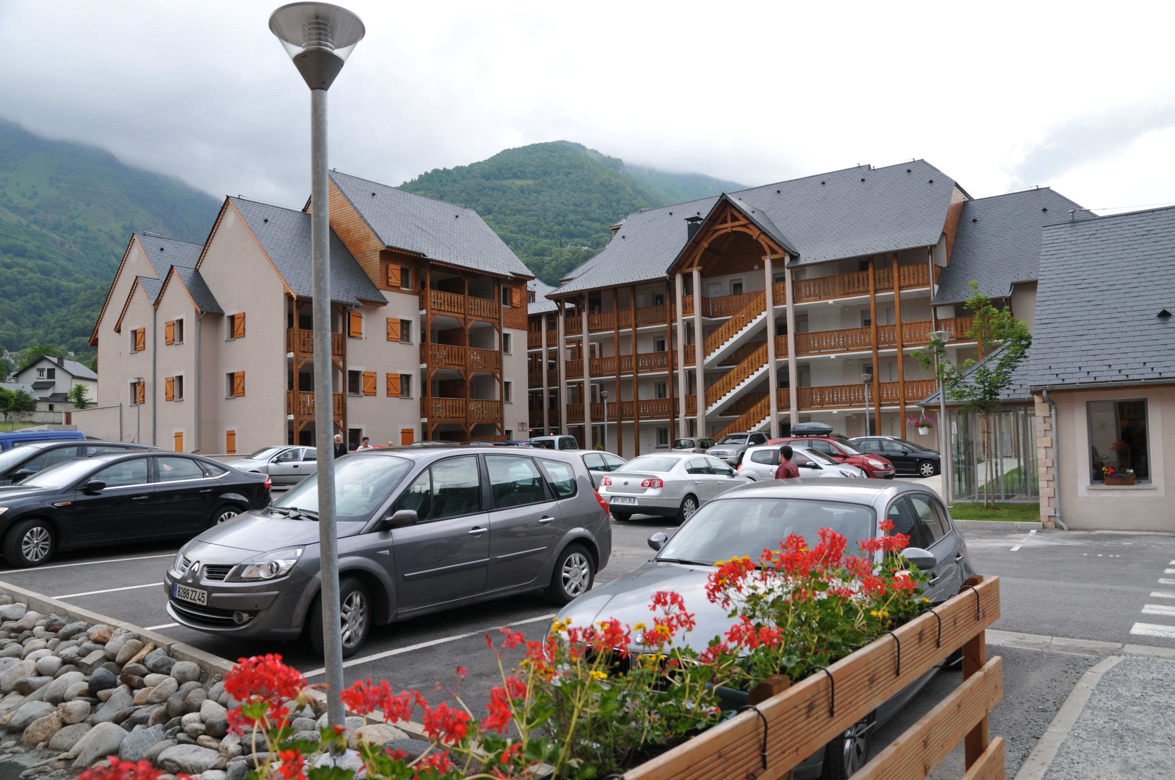 Un hotel con varios pisos, balcones y un estacionamiento lleno de coches.