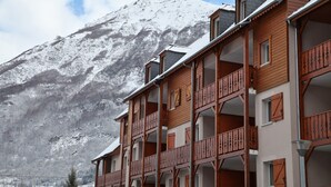 A wooden building with balconies, set against a snow-covered mountain. - Domaine Val de Roland (Luz-Saint-Sauveur)