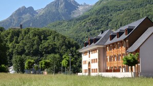 A traditional chalet-style building with multiple balconies, set against a backdrop of lush green mountains. - Domaine Val de Roland (Luz-Saint-Sauveur)