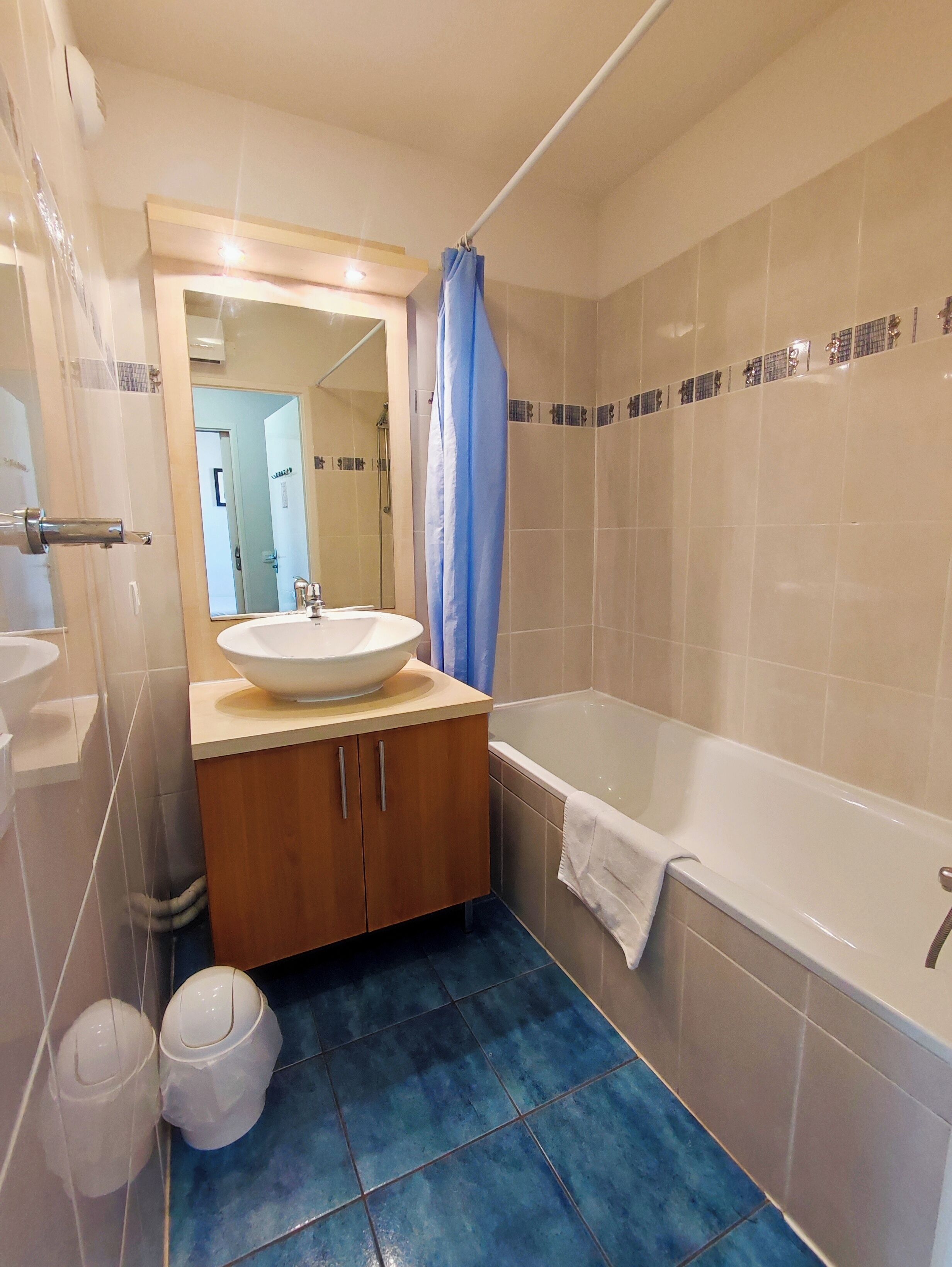 A bathroom with a sink, vanity, bathtub, and blue shower curtain.