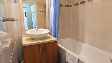 A bathroom with a sink, vanity, bathtub, and blue shower curtain.