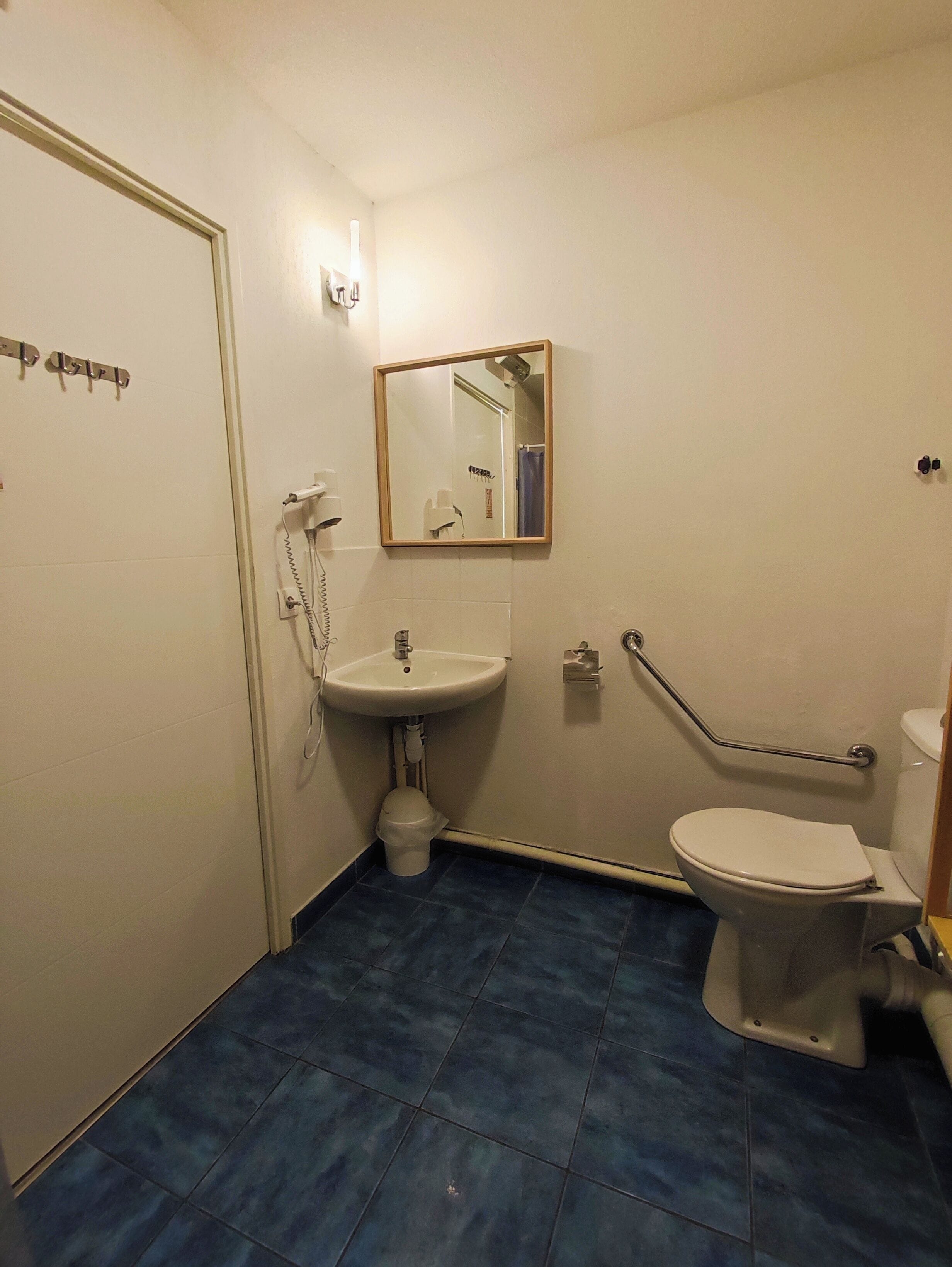 Un baño con un lavamanos blanco, un espejo, un inodoro y una barra de apoyo.