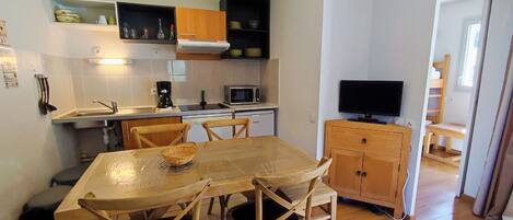 Une cuisine compacte avec un coin repas, des meubles en bois, un four à micro-ondes et un téléviseur.