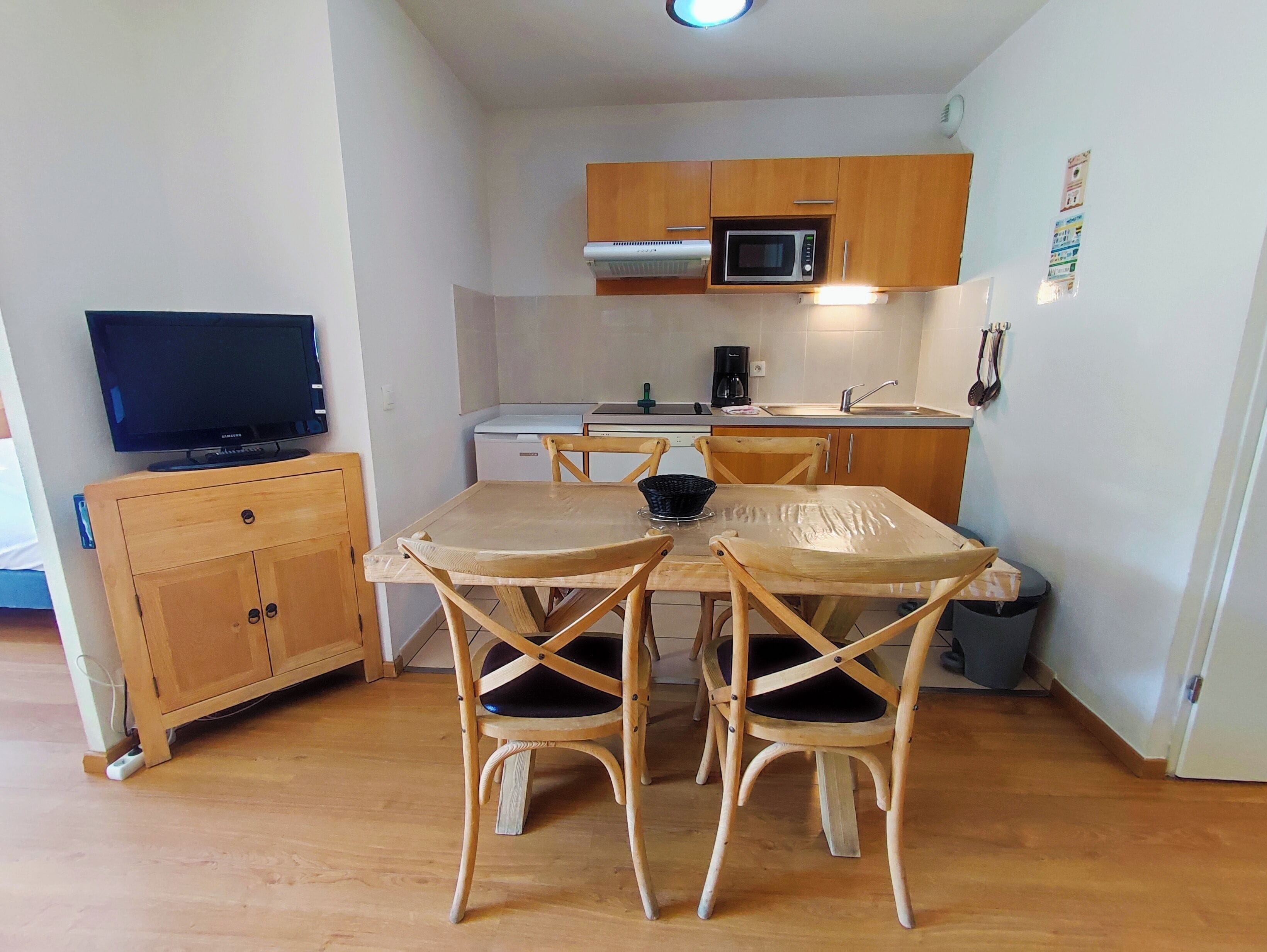 Une cuisine compacte dotée de meubles en bois, d’un four à micro-ondes, d’une machine à café et d’une table à manger avec quatre chaises.