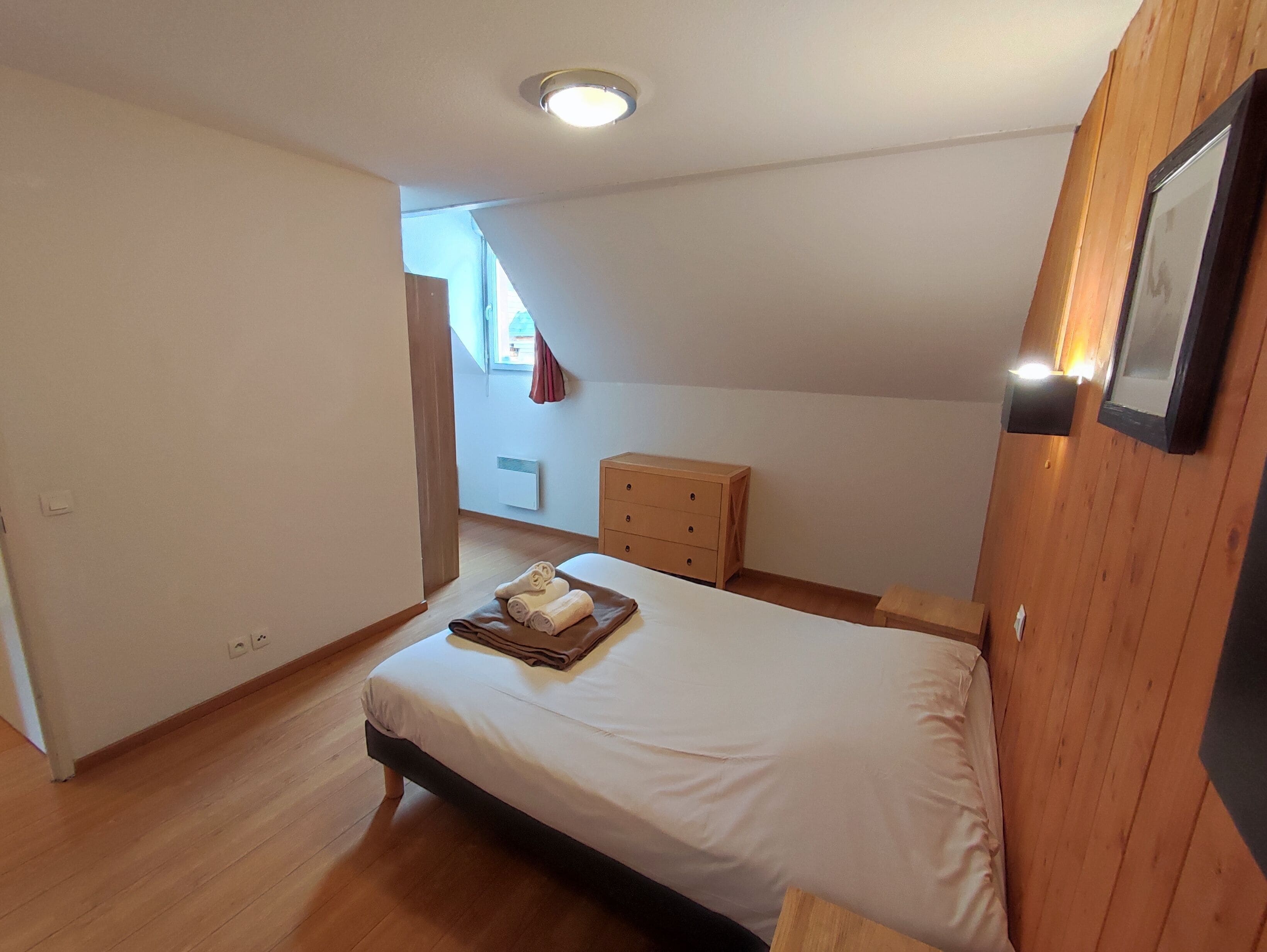Un dormitorio con cama, cómoda de madera y lámpara en el techo.