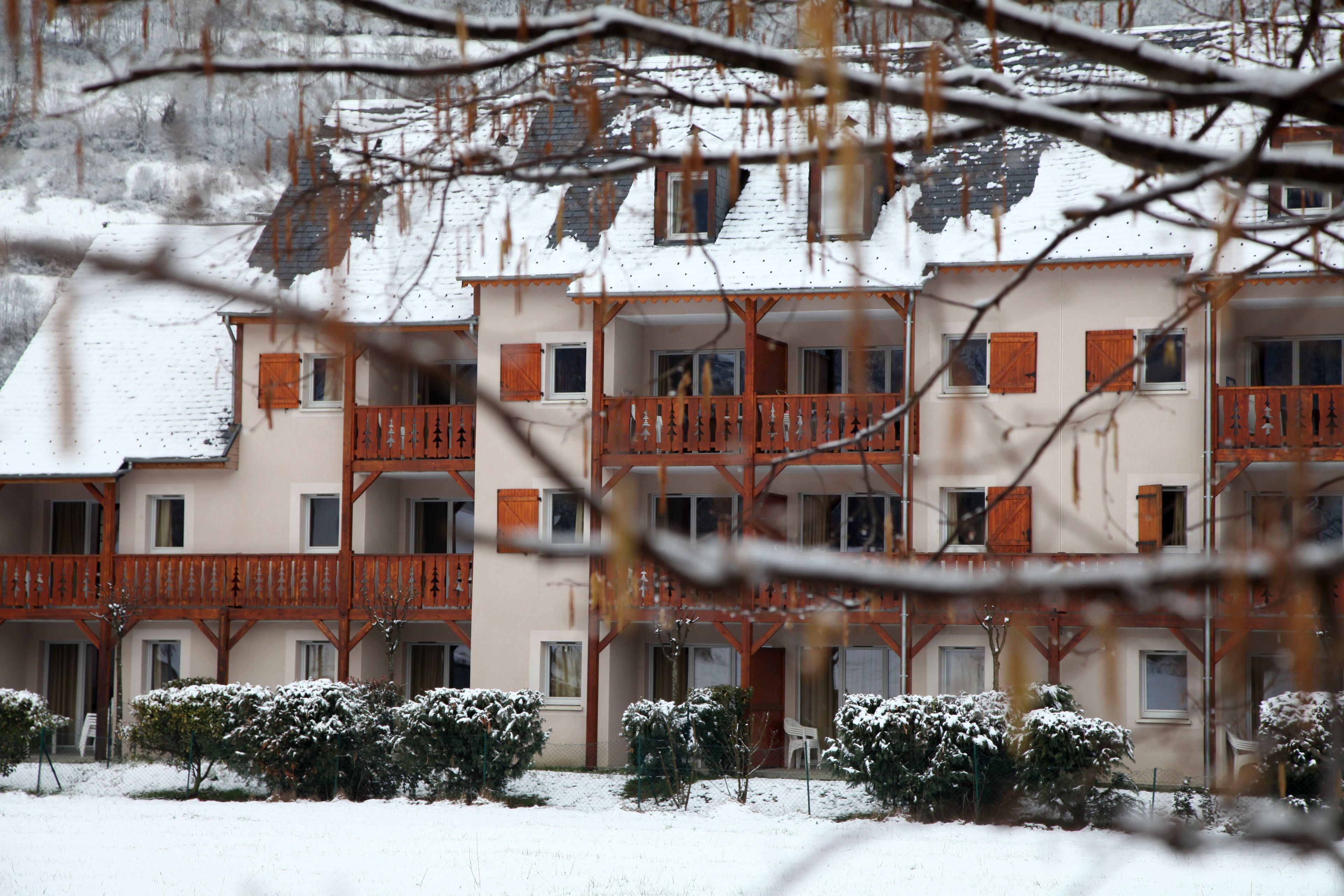 Un immeuble à plusieurs étages, doté de balcons et de fenêtres, entouré d’arbustes couverts de neige.