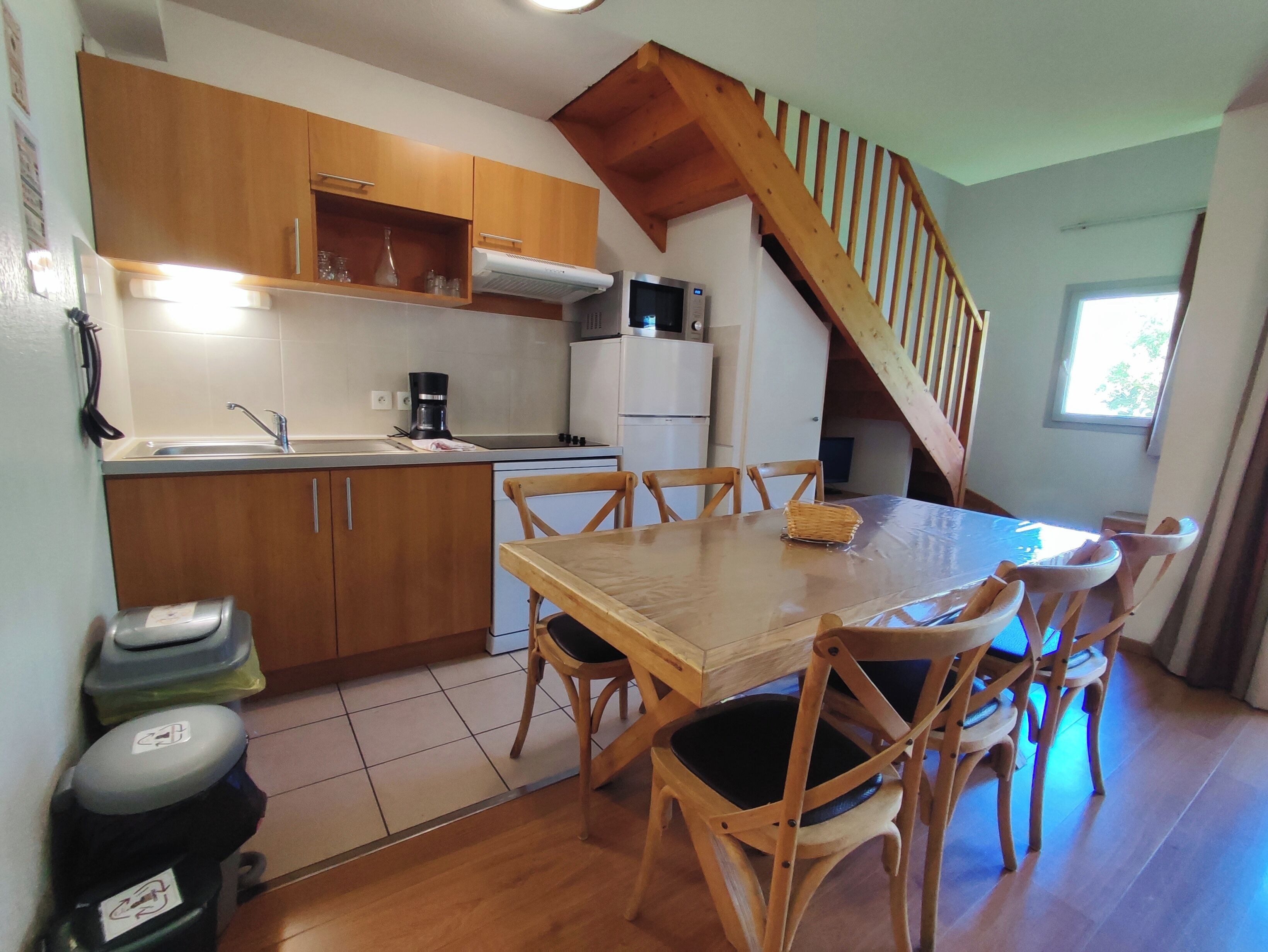 Una cocina funcional con armarios de madera, una mesa de comedor con sillas, una estufa integrada y una escalera de madera.