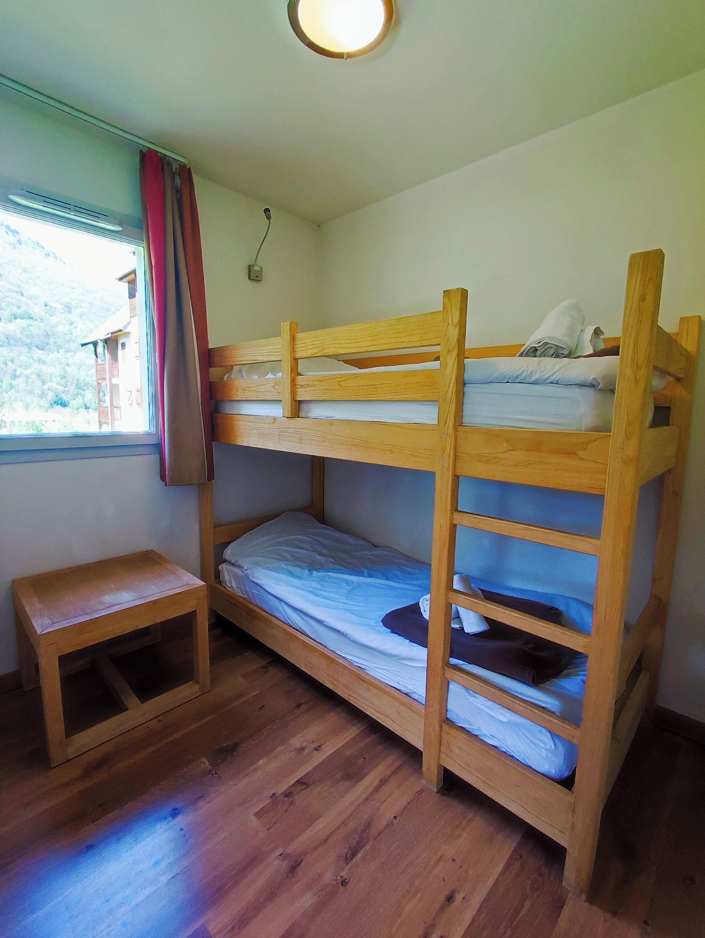 Un letto a castello con struttura in legno, un tavolino in legno e una finestra con tende.