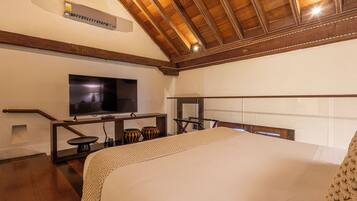 A hotel room with a large bed, a flat-screen TV mounted on the wall, wooden beams on the ceiling, and a small table with decorative bowls.