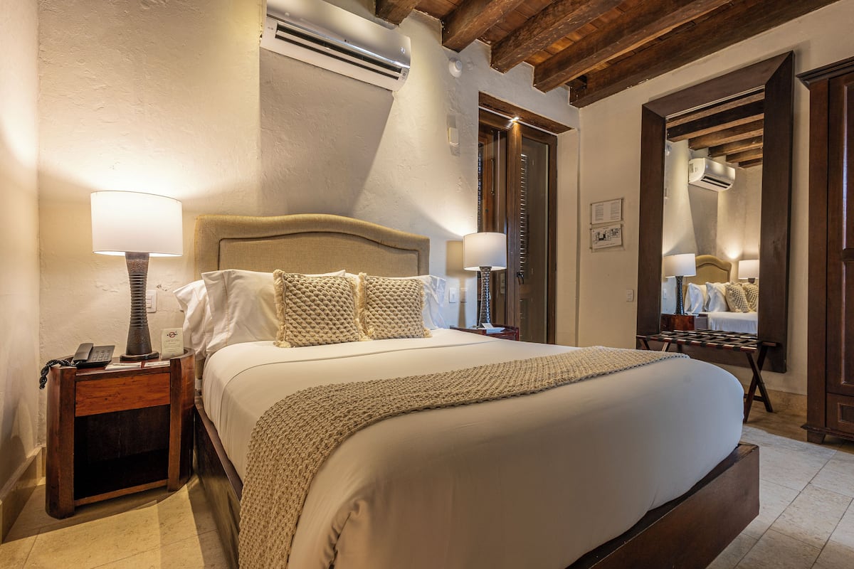 A well-lit bedroom with a large bed, wooden headboard, bedside lamps, and a wooden bench.