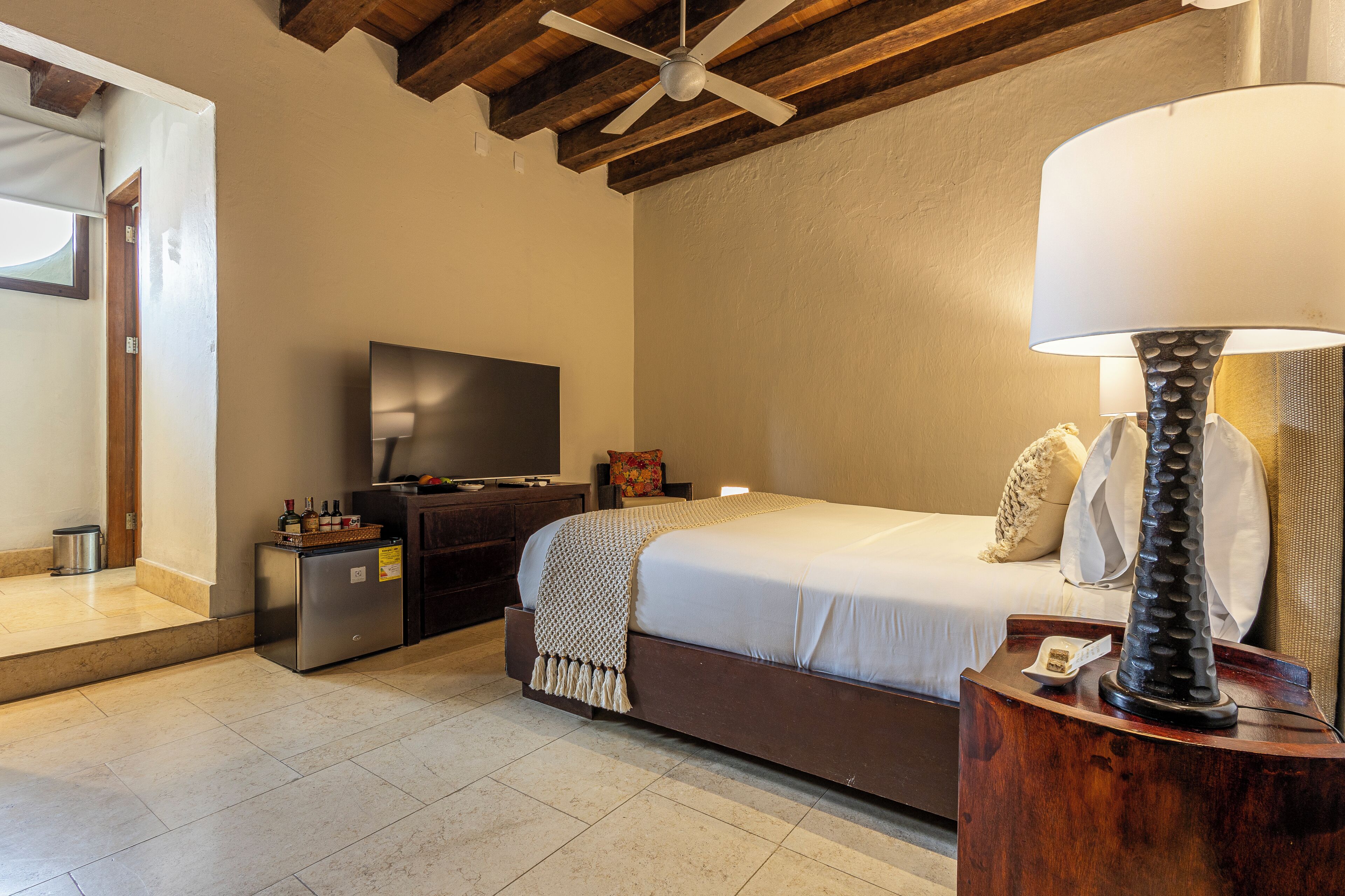 Un dormitorio con cama, televisión, lámpara y techo de madera.