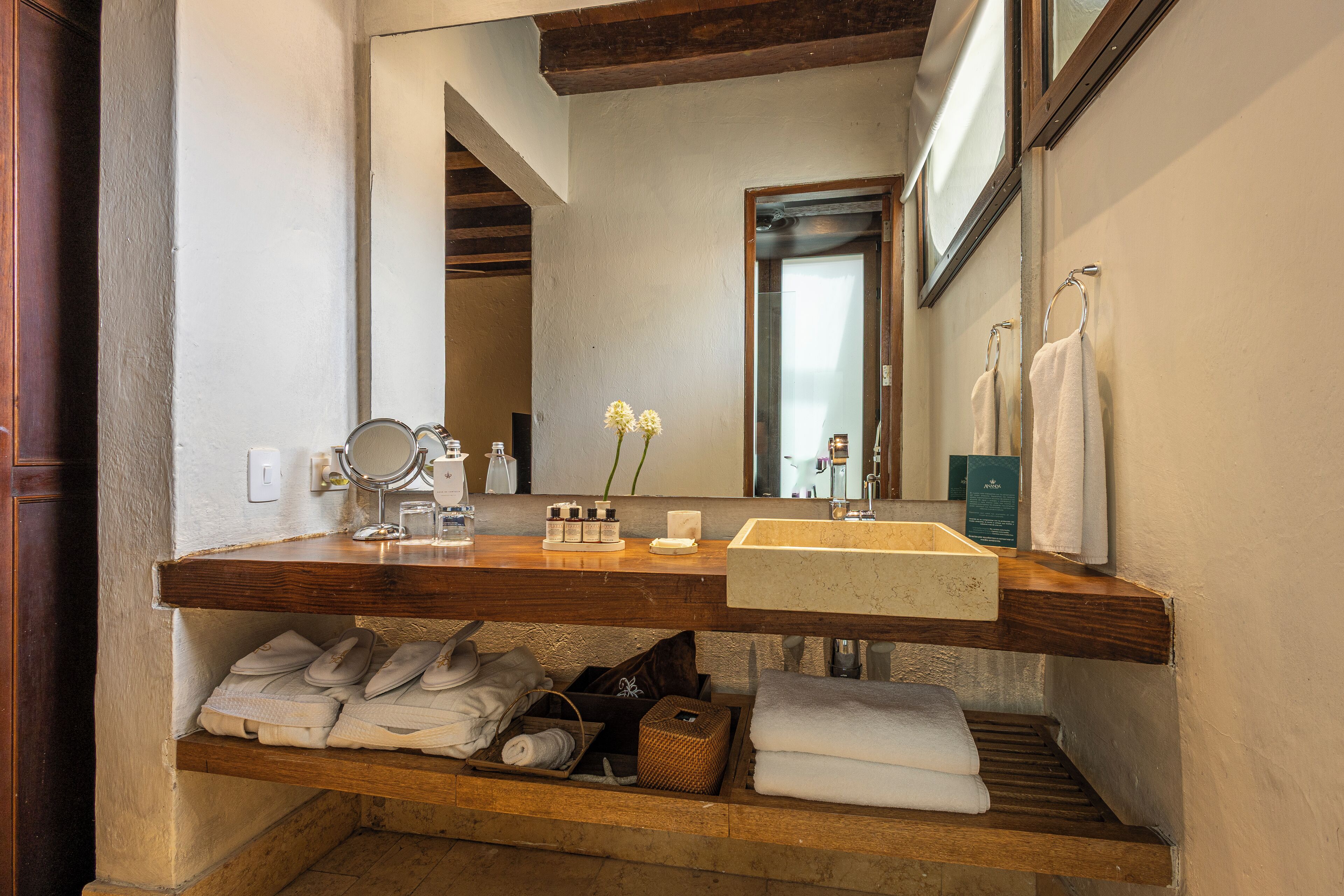 A bathroom with a wooden vanity, a large mirror, a sink, and shelves with towels and toiletries.
