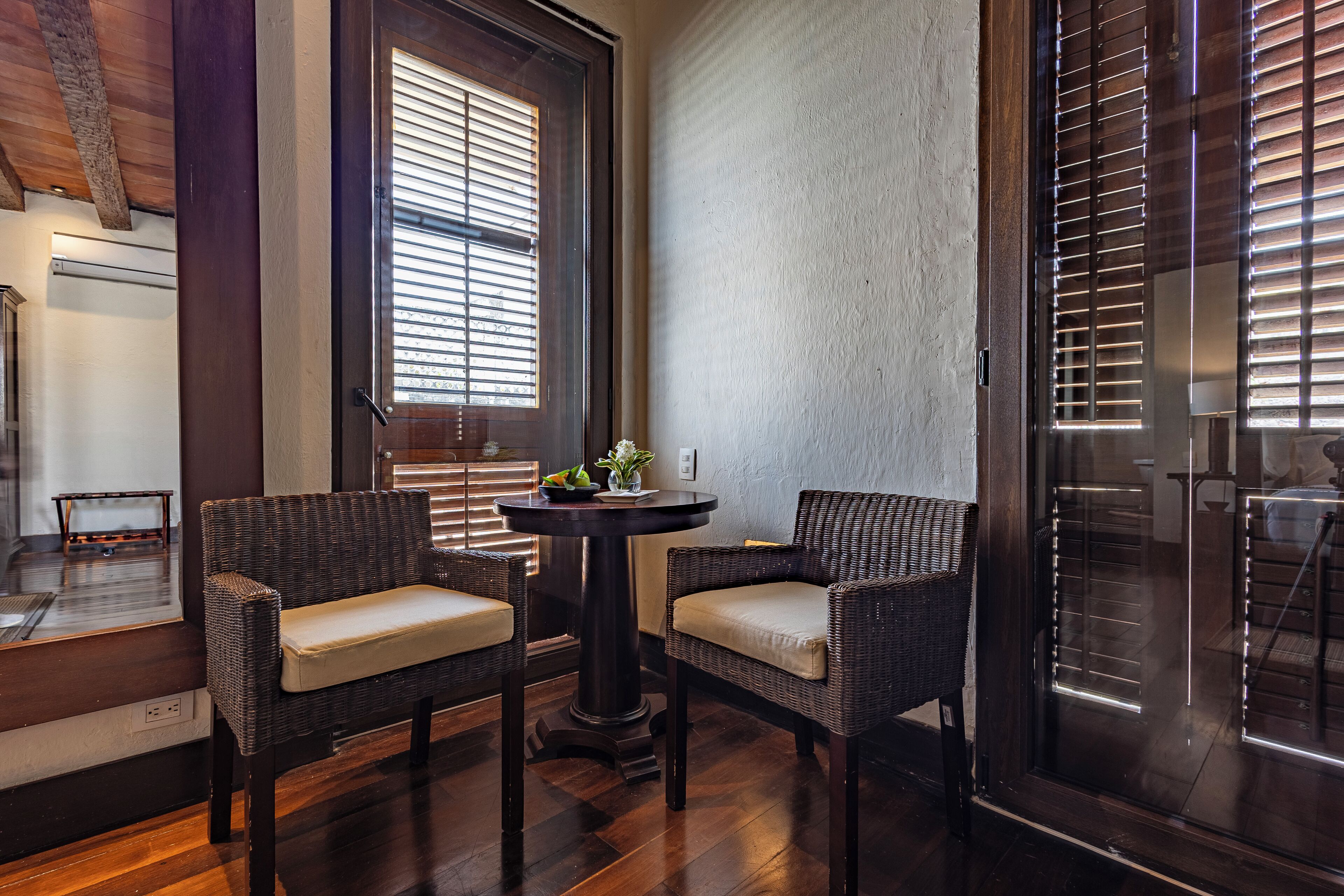 A corner room with wicker chairs, a round table, and a window with blinds.