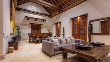 A spacious living area with a high ceiling, wooden beams, a sofa set, a dining table, and a large mirror.
