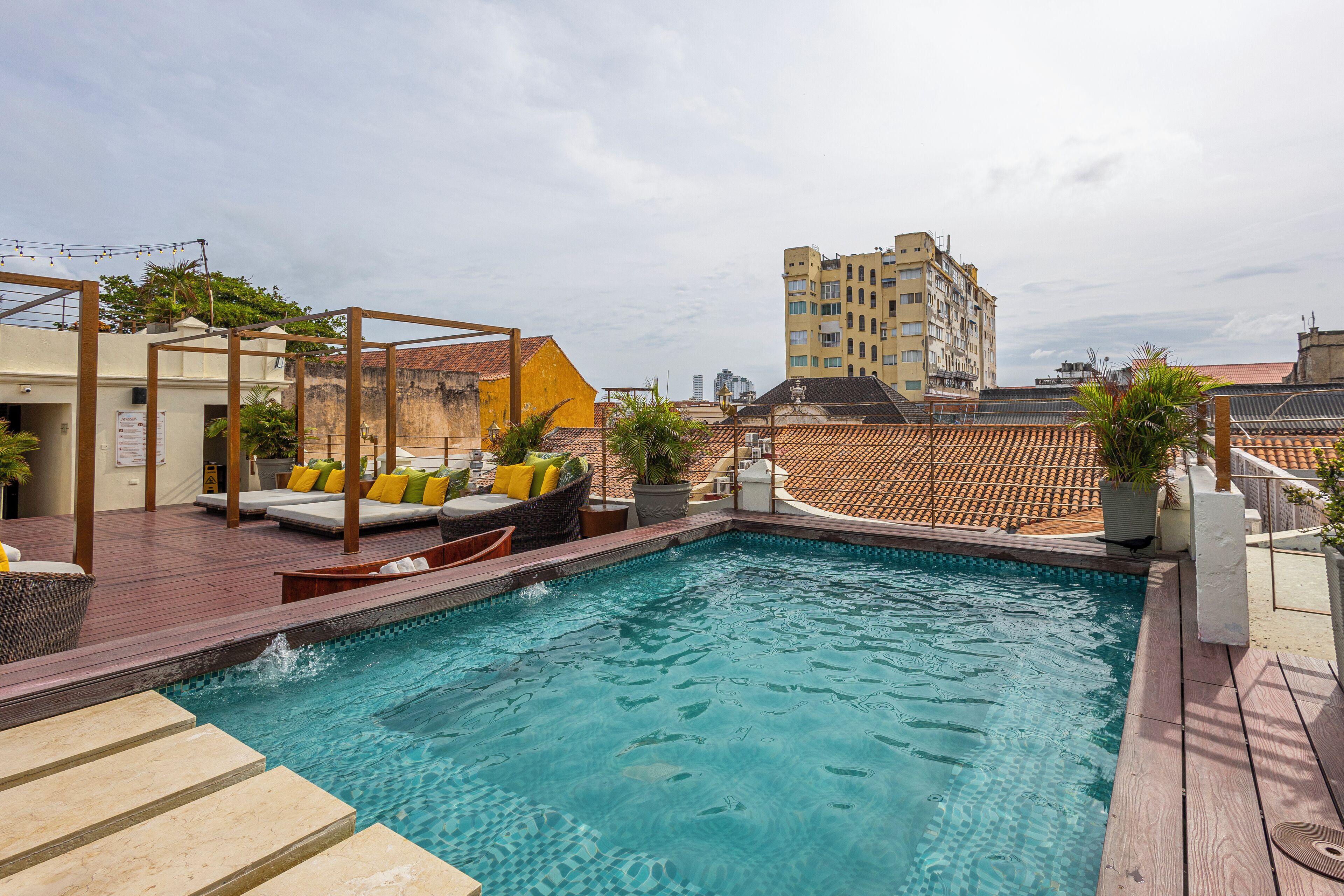A rooftop pool with wooden deck, outdoor seating, and potted plants.