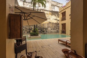 Un espace aménagé au bord de la piscine, avec un sol carrelé, des chaises longues, un fauteuil en osier et un grand parasol.