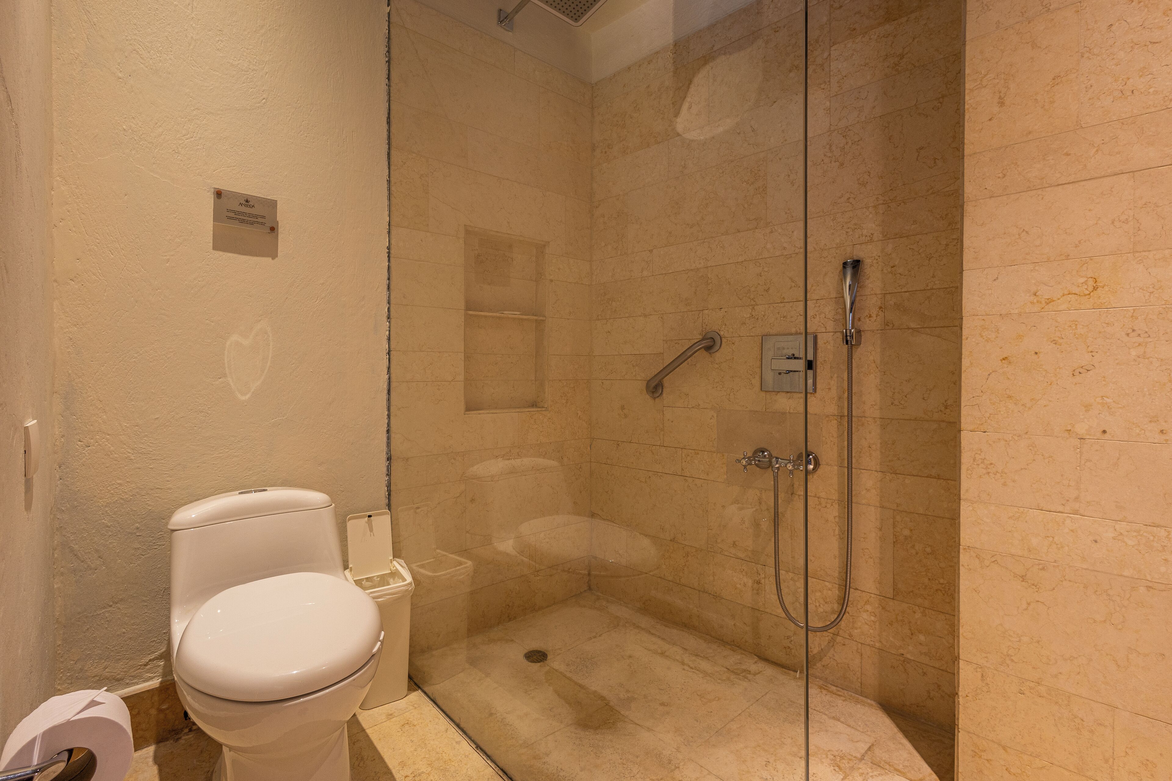 A bathroom with a toilet, a glass-enclosed shower, and a marble-tiled wall.