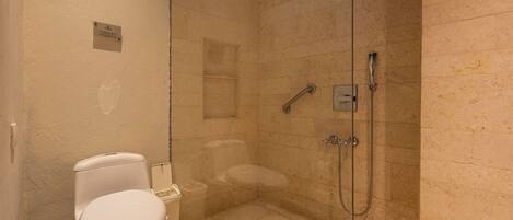 Un baño con inodoro, ducha con mampara de vidrio y pared con azulejos de mármol.