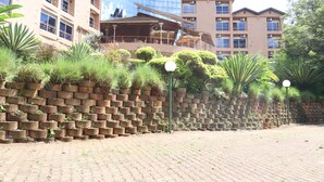 A hotel with a brick wall adorned with greenery, a paved walkway, and a modern building in the background. - Metropole Hotel Kampala (Kampala)