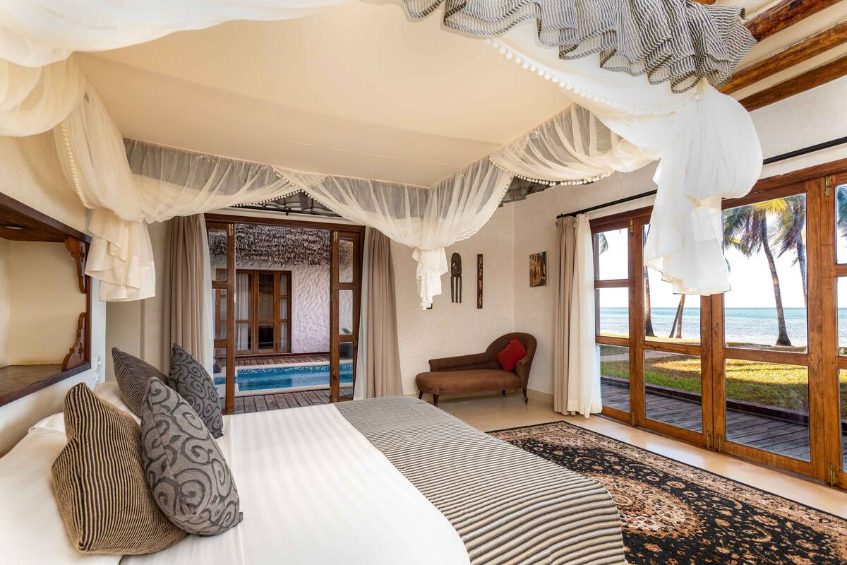 A bedroom with a large bed, a view of the ocean, and a balcony with a view of palm trees.