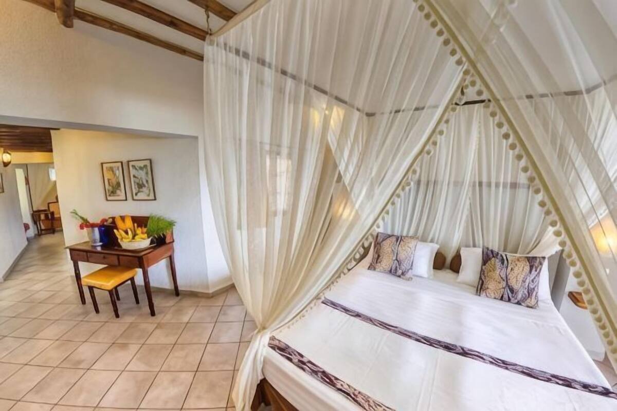 A bedroom with a canopy bed, a desk with a chair, and a view of the hallway.