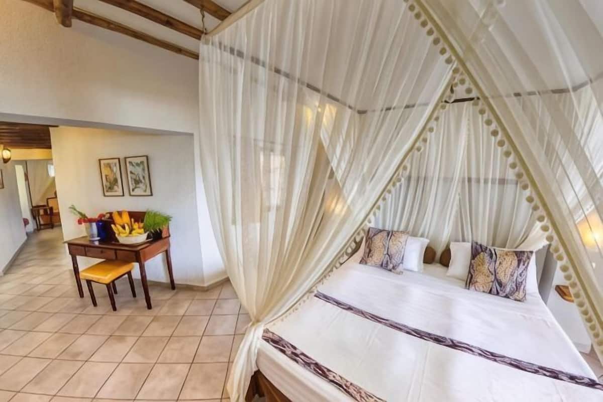 A bedroom with a canopy bed, a desk with a chair, and a view of the hallway.