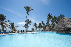 A clear blue pool surrounded by lounge chairs and palm trees, with a thatched-roof structure in the background. - Karafuu Beach Resort & Spa (Michamvi)