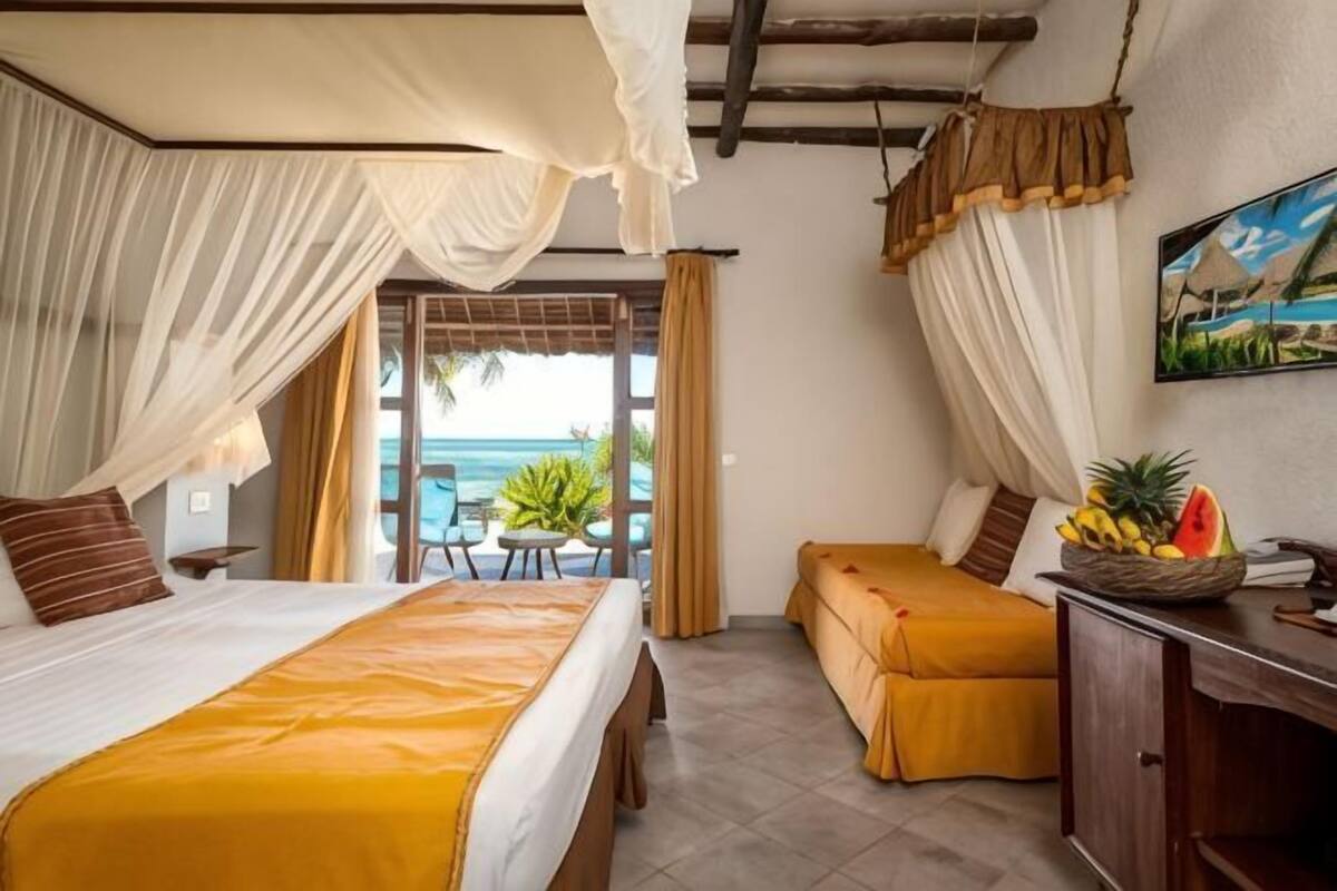 A hotel room with two beds, a balcony with a view of the sea, and a dining area with a table and chairs.