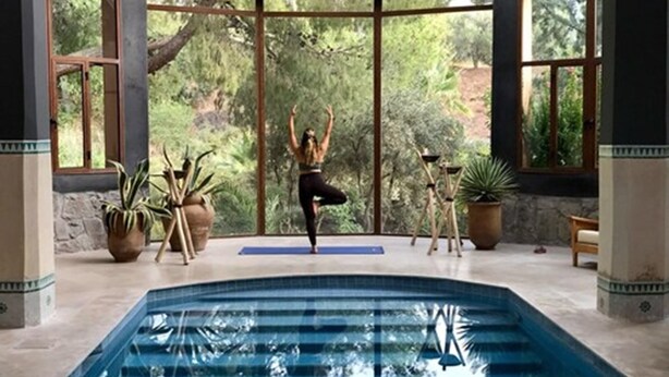 Una colchoneta de yoga en una habitación con un ventanal grande, una piscina y plantas en macetas.