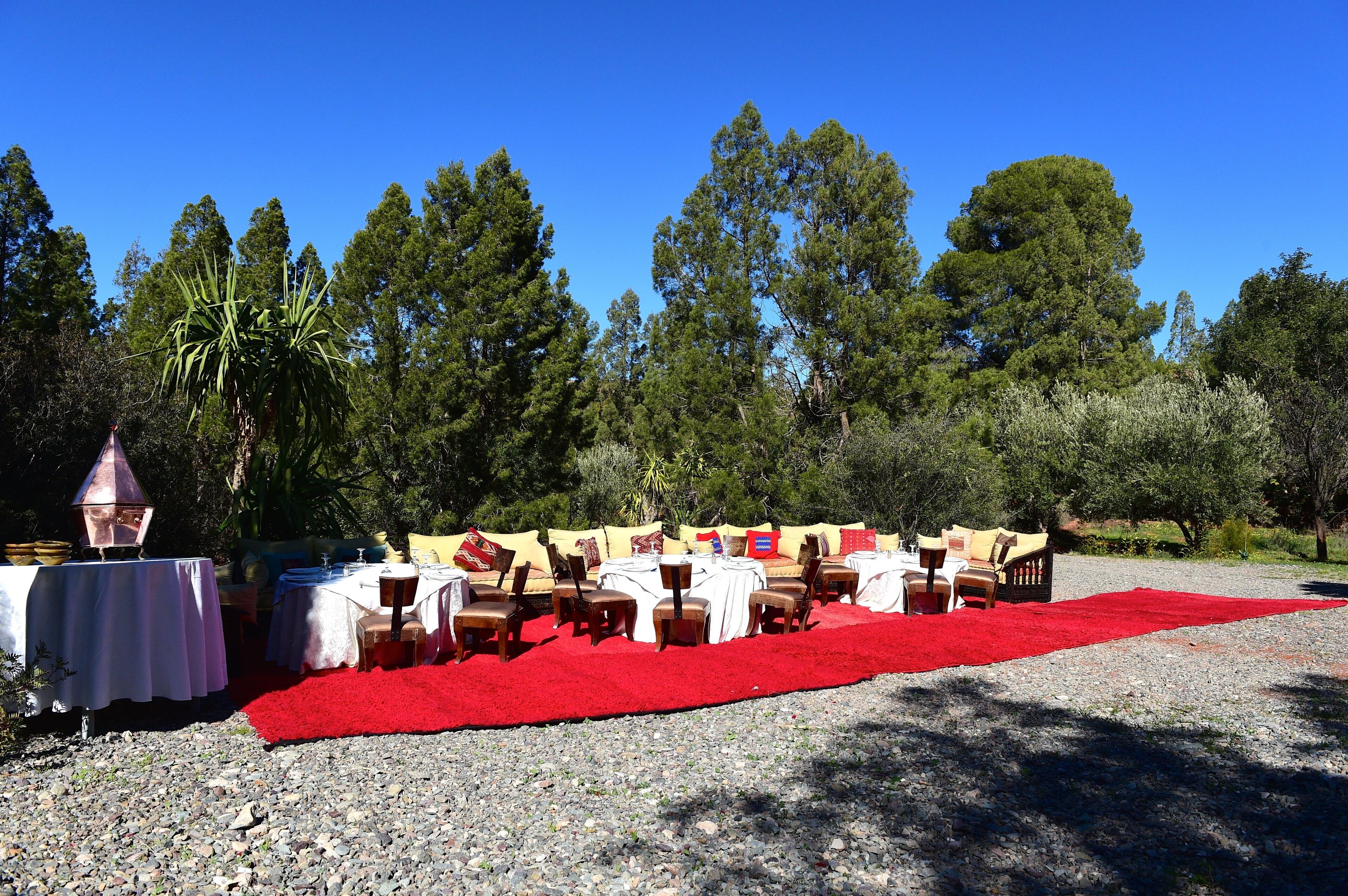 Un espace extérieur aménagé avec des tables et des chaises disposées sur un sol de gravier, entouré d’arbres.