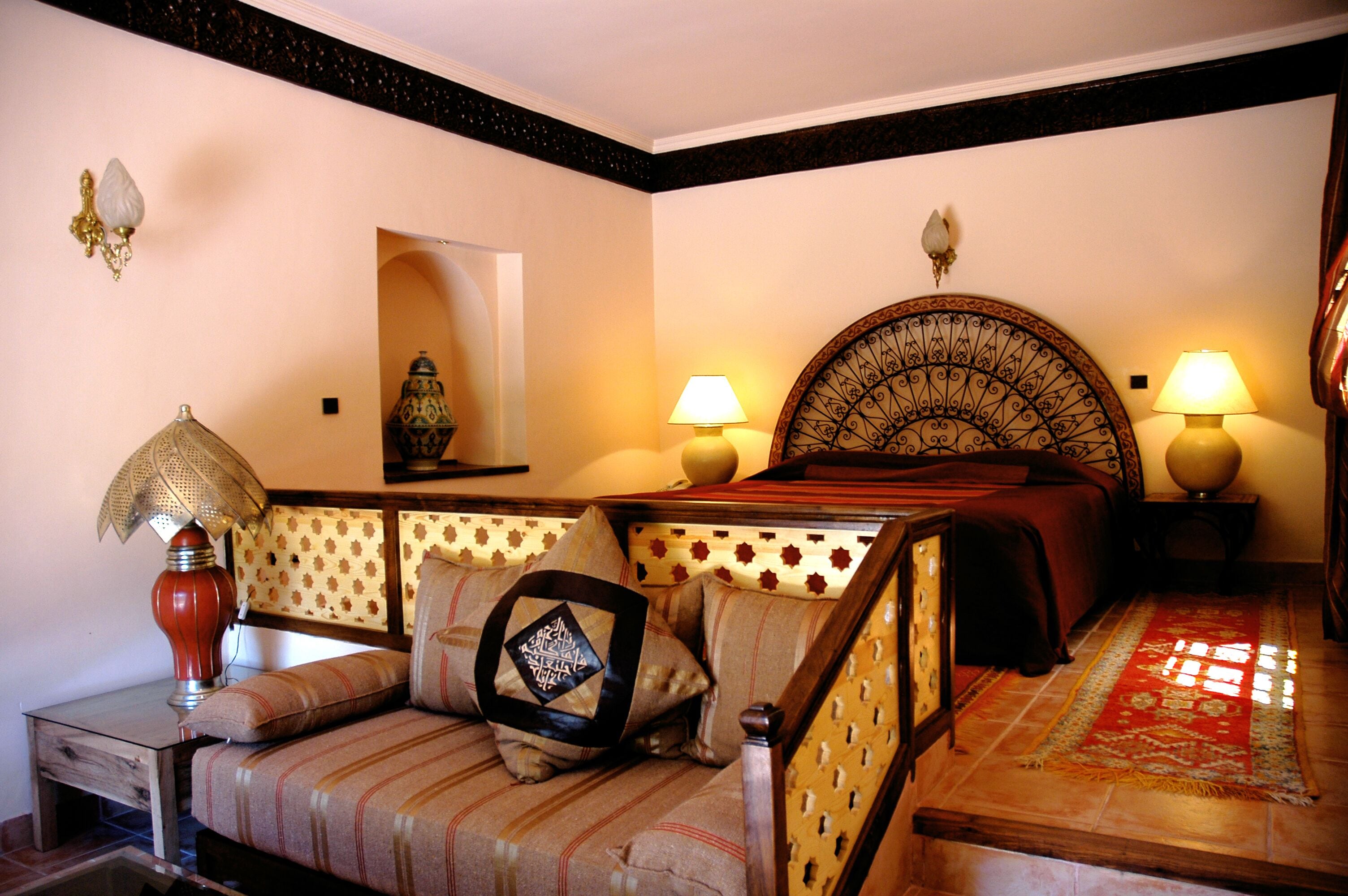A traditional room with a bed, a sofa, two wall-mounted lamps, and a decorative wall piece.