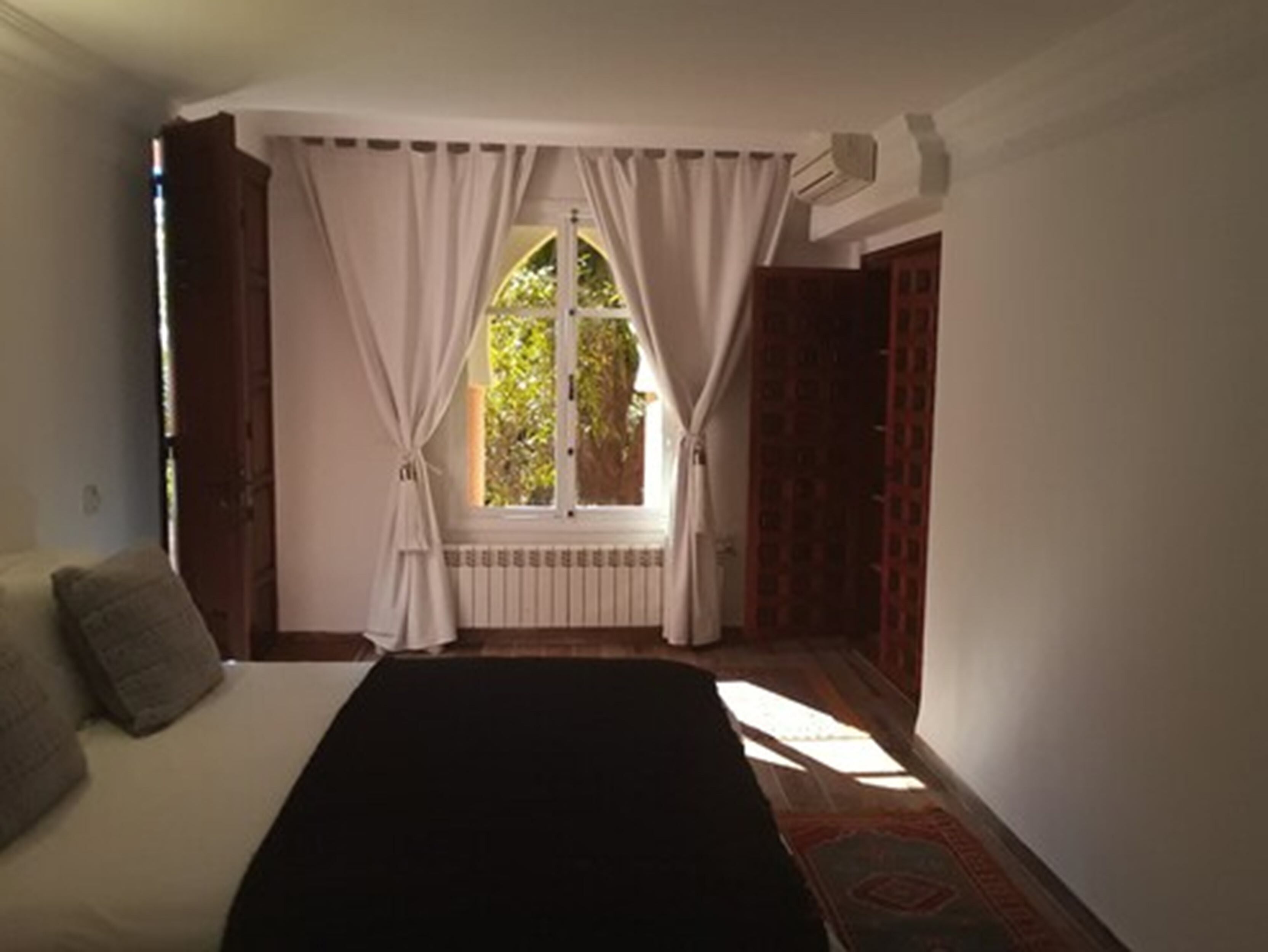 A bedroom with a bed, a window with curtains, a radiator, and a patterned rug.