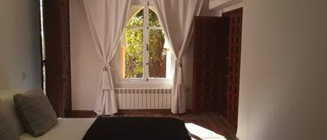 A bedroom with a bed, a window with curtains, a radiator, and a patterned rug.