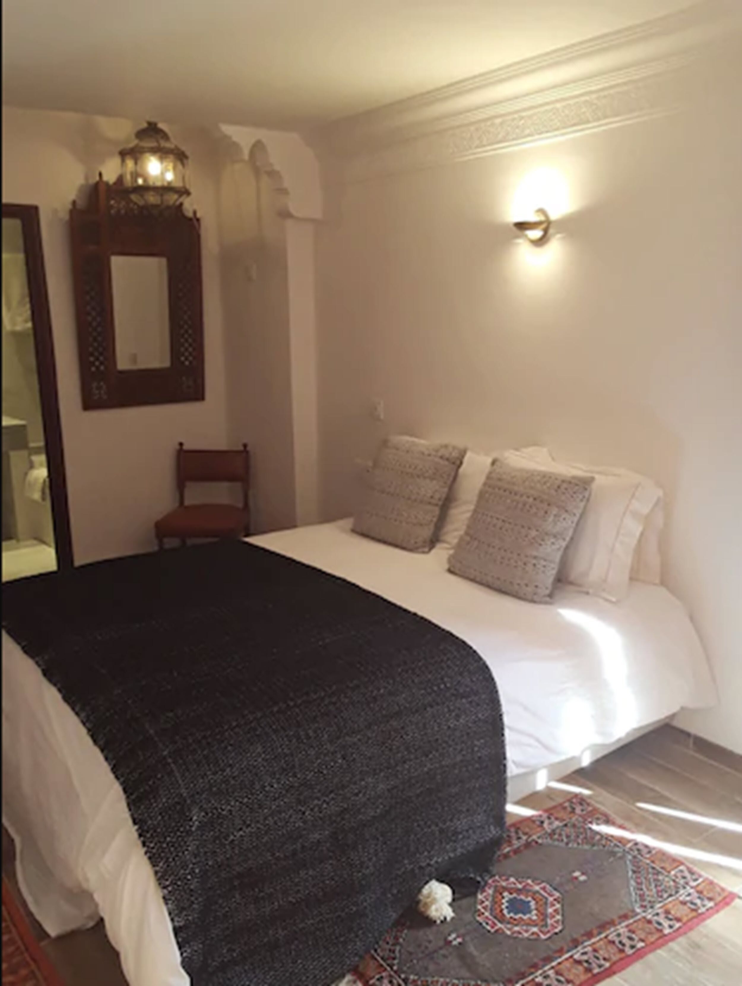 Un dormitorio con cama, una silla, un espejo y una lámpara de pared.