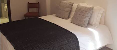Un dormitorio con cama, una silla, un espejo y una lámpara de pared.
