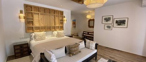 Une chambre à coucher avec un grand lit, une tête de lit en bois, des tables de chevet, une commode, un miroir et des tableaux encadrés accrochés au mur.