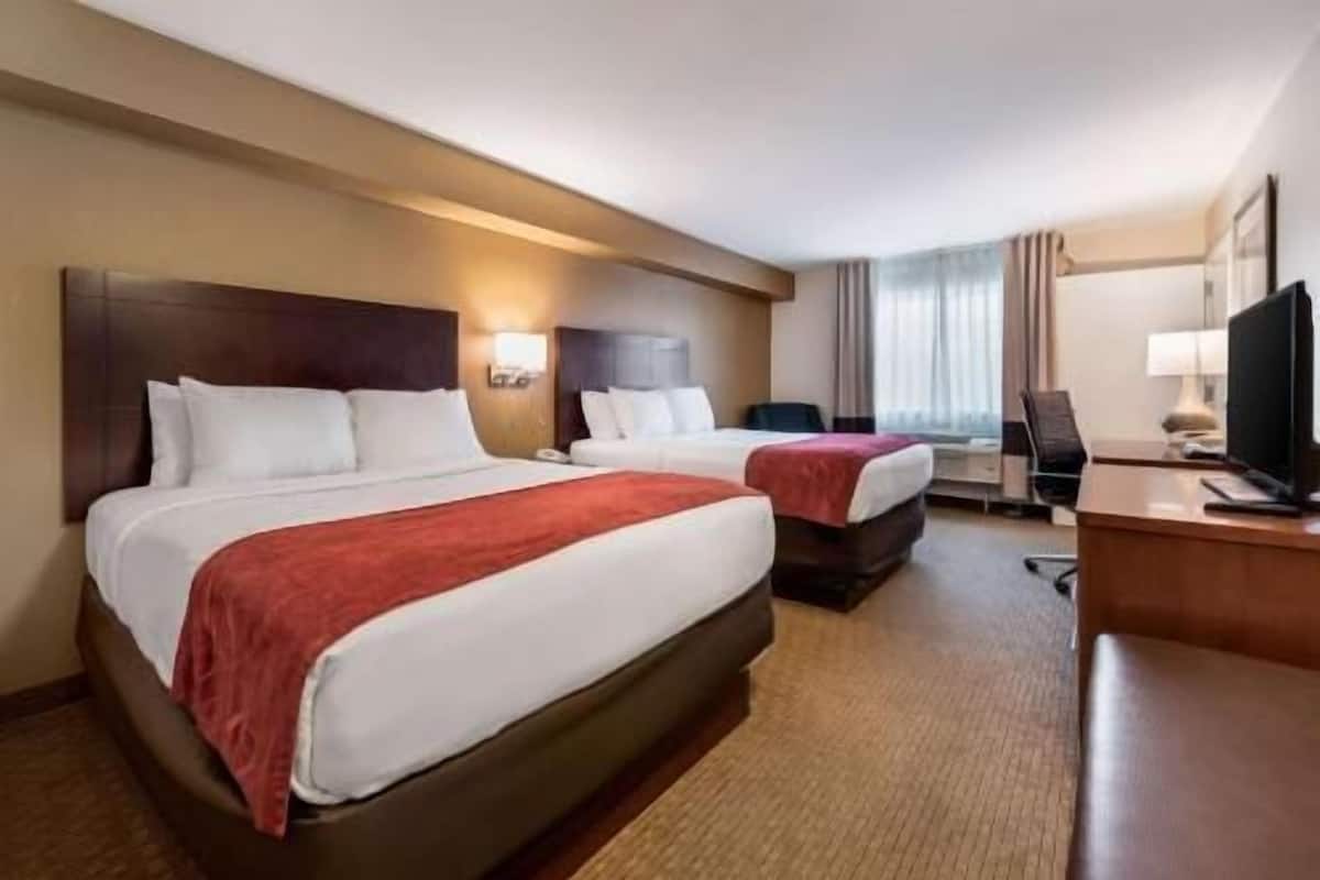 Una habitación de hotel con dos camas, un escritorio, una silla y un televisor.