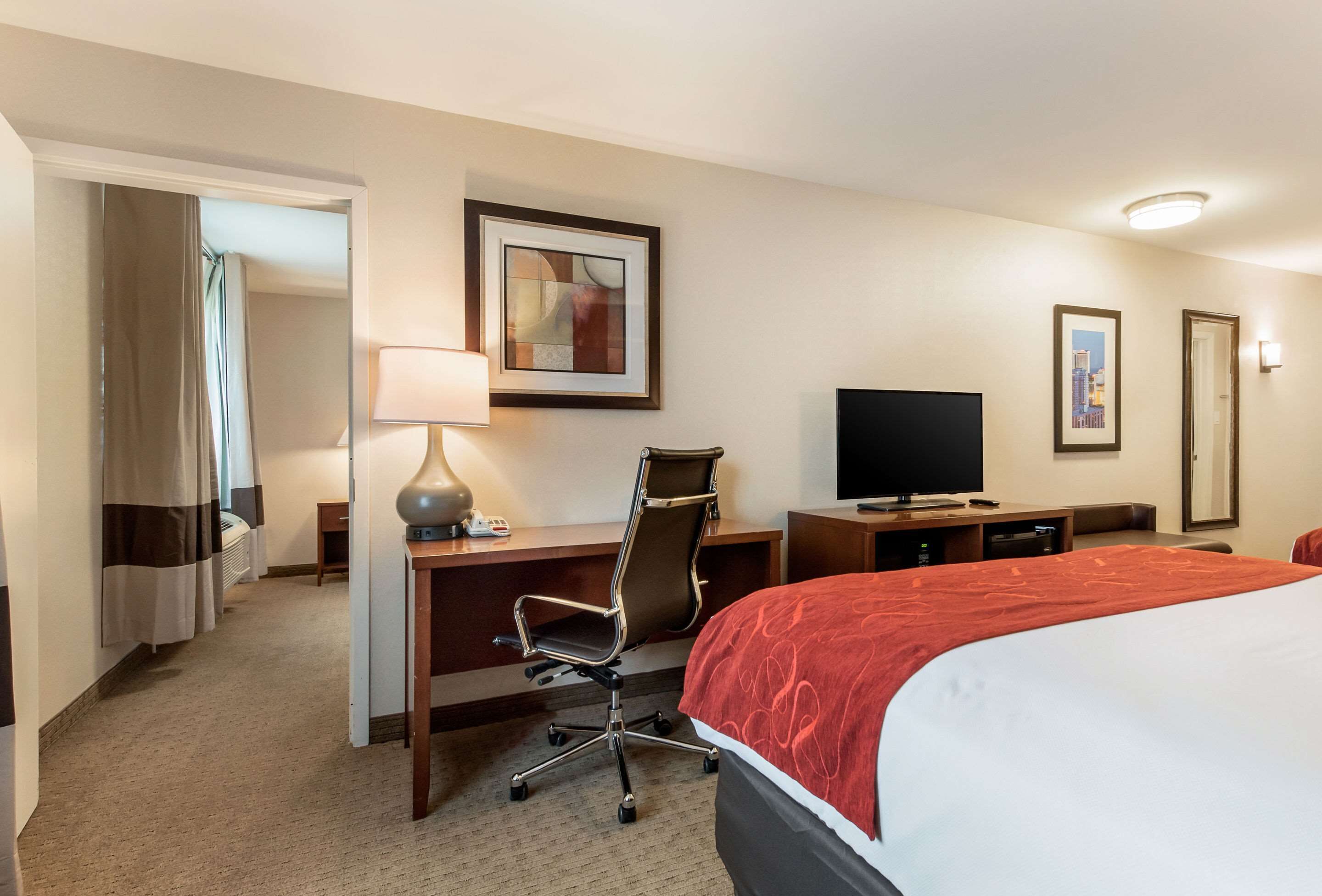 A hotel room with a bed, desk, chair, TV, and artwork on the walls.