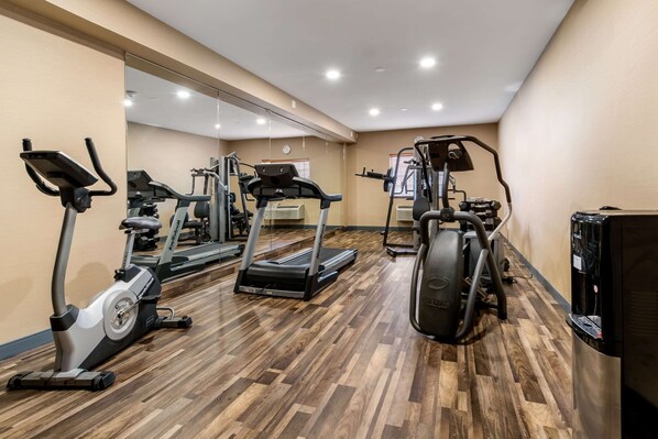 Une salle de sport équipée de matériel d’exercice, d’un distributeur d’eau et d’un mur entièrement recouvert de miroirs.