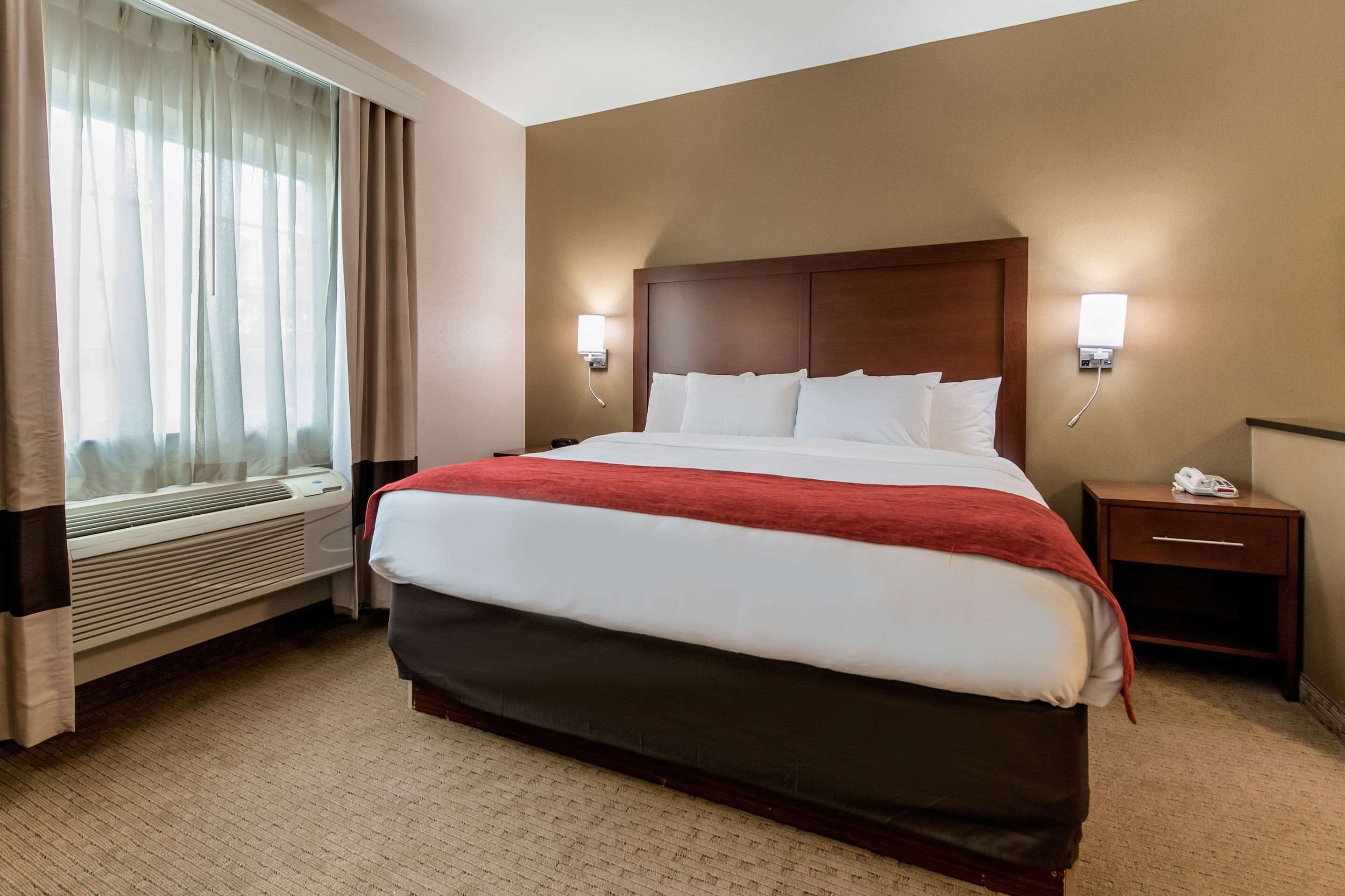 A hotel room with a large bed, a bedside table with a phone, and a window with curtains.