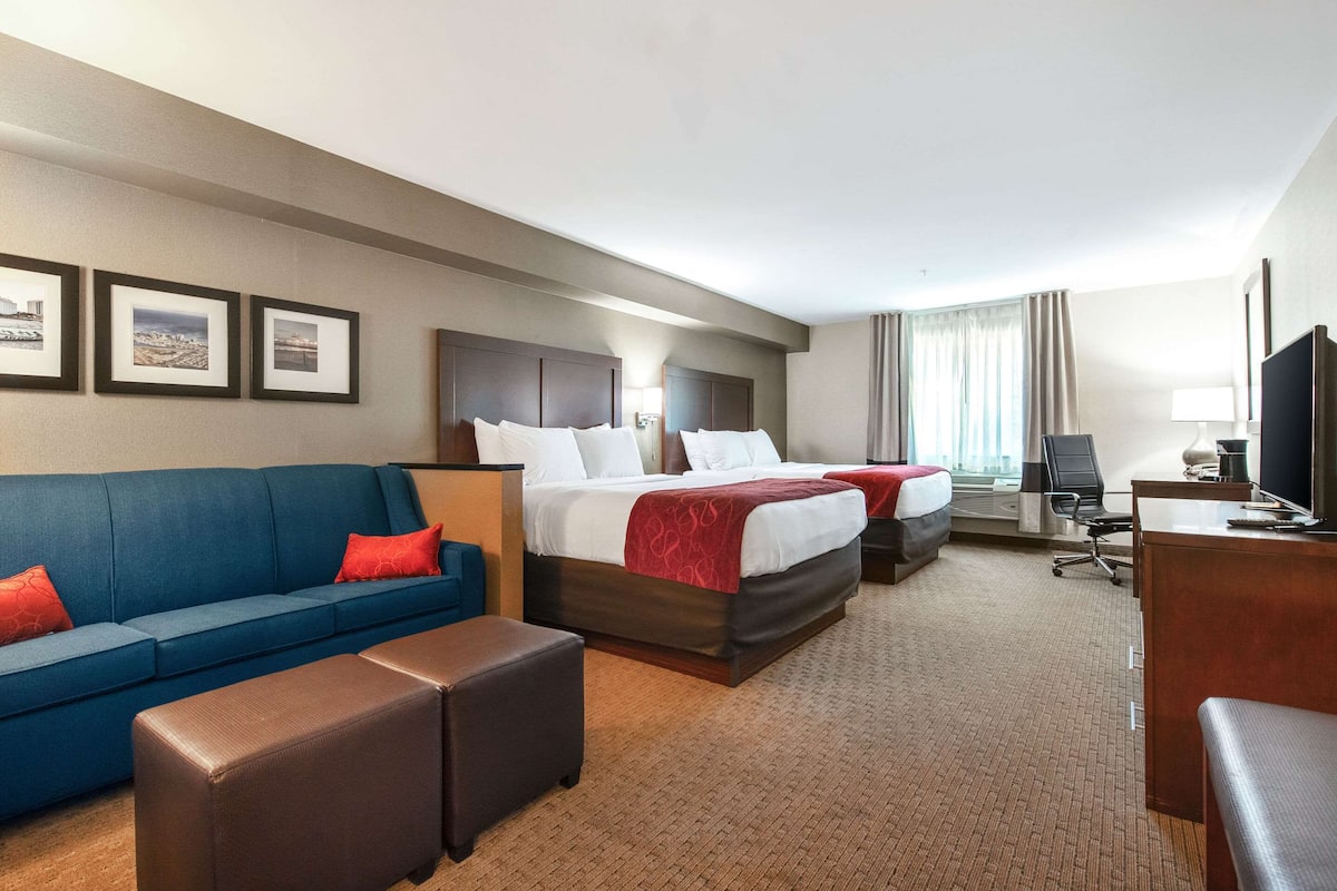 Una habitación de hotel con un sofá azul, dos camas, un escritorio y un televisor.