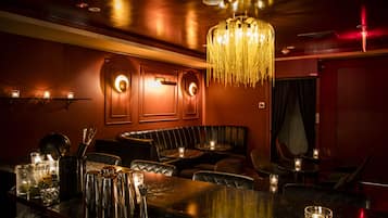 A bar area with a dark wood bar, cushioned seating, and a chandelier.