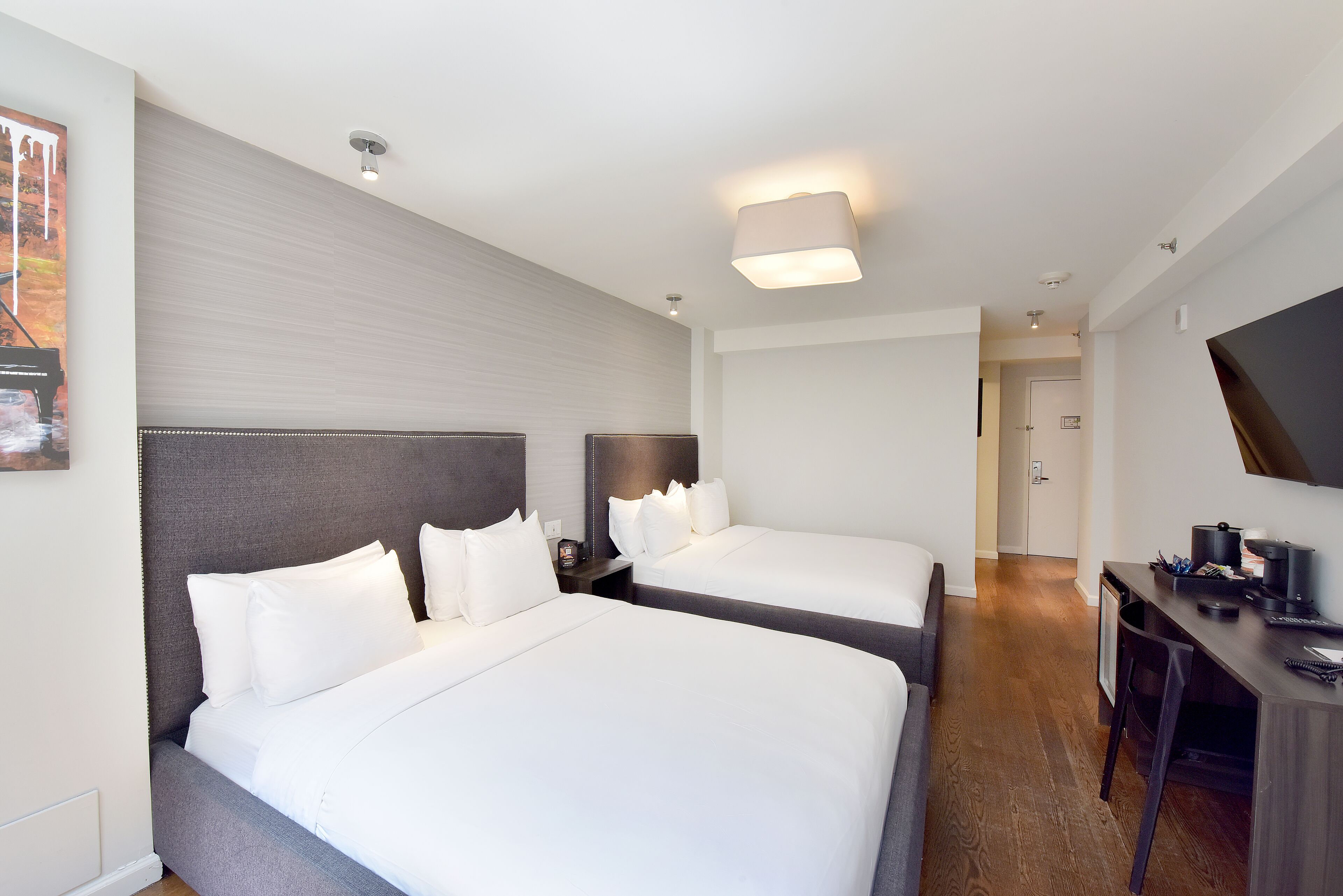 Habitación de hotel con dos camas, un escritorio con silla, un televisor y un cuadro en la pared.