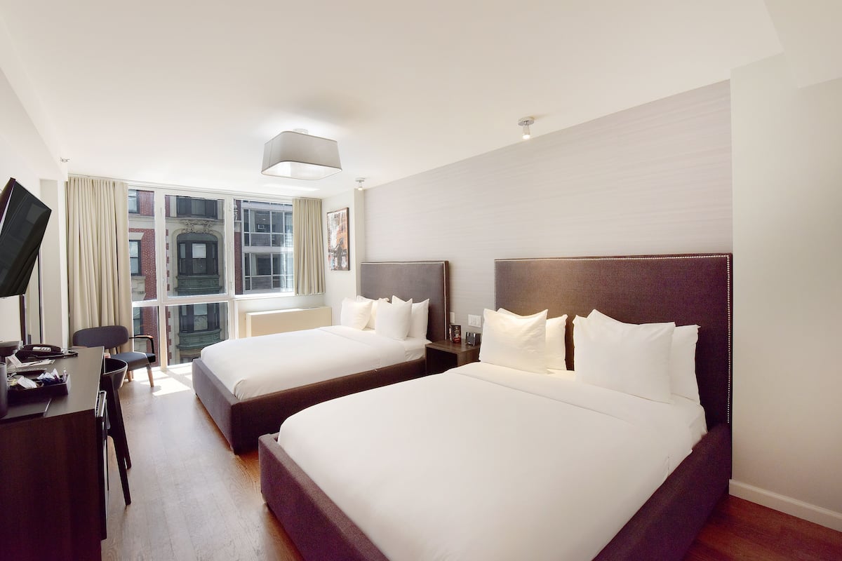 Una habitación de hotel con dos camas, un escritorio, una silla y un televisor.