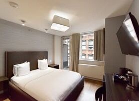 Una habitación de hotel con una cama grande, un escritorio con televisión de pantalla plana, una ventana con cortinas y vistas a un edificio de ladrillo.