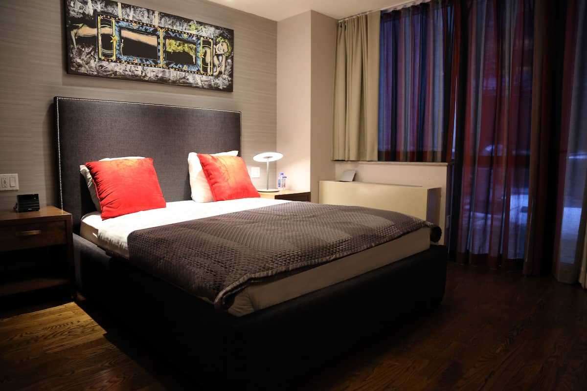 Una habitación de hotel con una cama grande, una mesita de noche, una lámpara, un espejo y una ventana con cortinas.