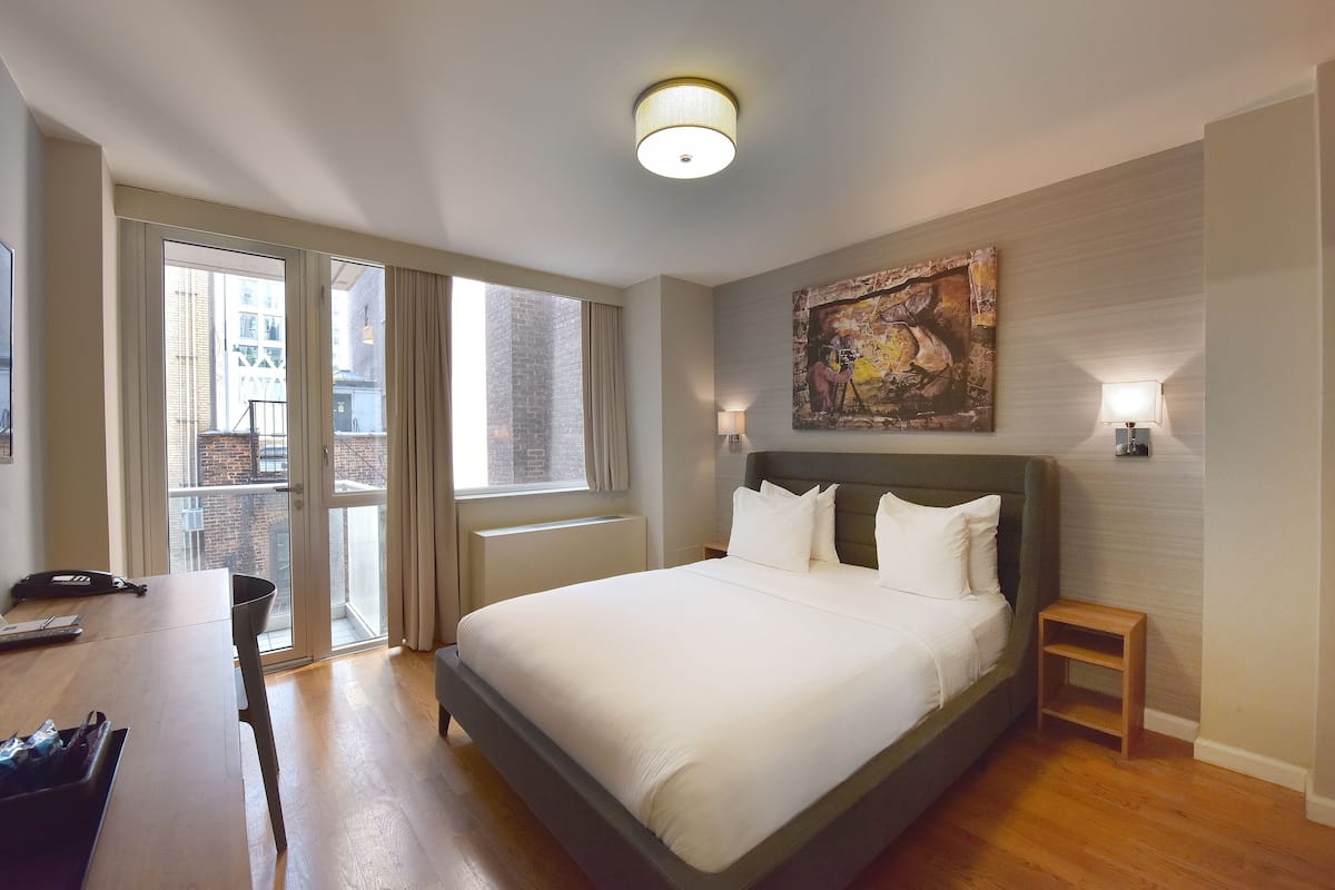 Una habitación de hotel moderna con una cama grande, un escritorio y vistas de la ciudad a través de las puertas del balcón.