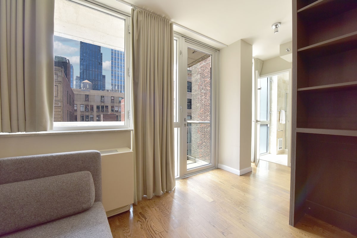 Un apartamento moderno con un ventanal grande, puerta corrediza al balcón y estantería empotrada.